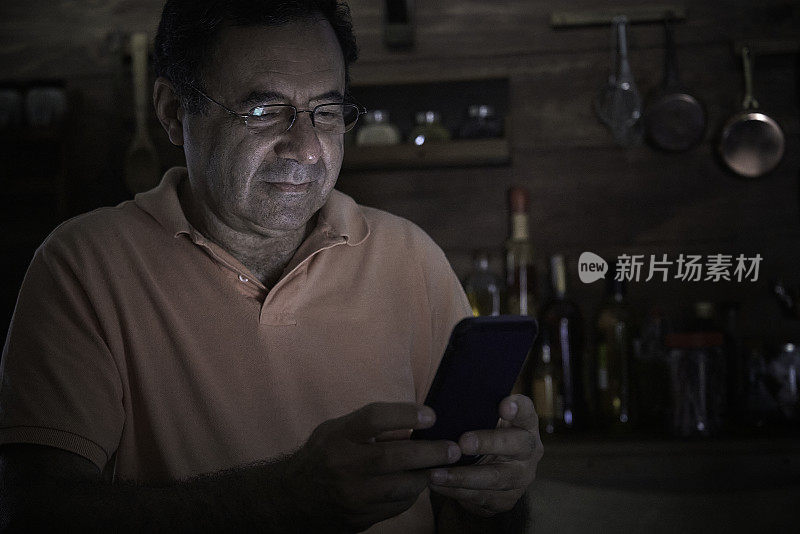 西班牙裔老人在昏暗的家庭厨房里使用智能手机