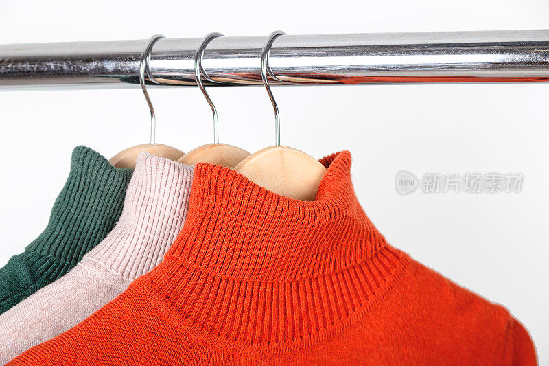 基本的秋季女性衣橱概念。挂在衣架上的空白高领毛衣。明亮的橙赭色卷领与米色和绿色。