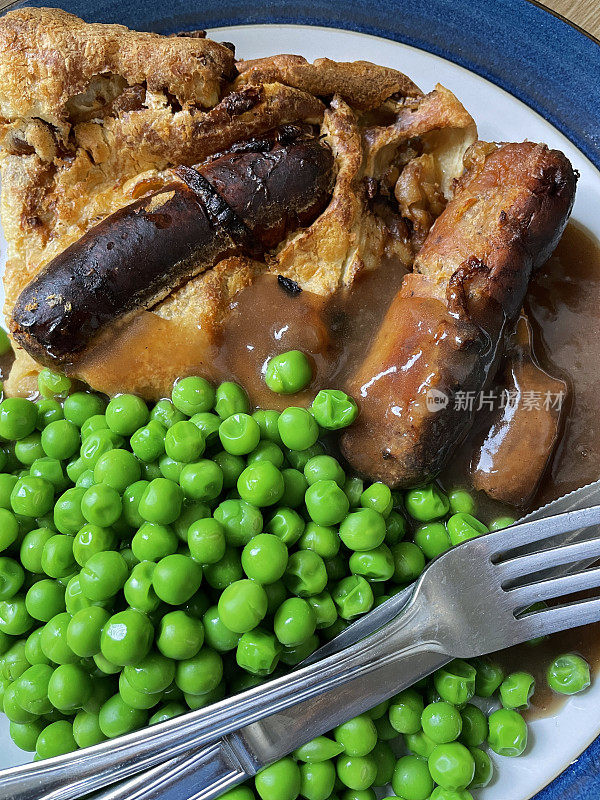 全画框图像自制的传统英国蟾蜍在洞食谱与多汁的猪肉香肠，约克郡布丁面糊和焦糖洋葱，青豆和肉汁在白色盘子与蓝色的边缘，刀和叉，提高视野