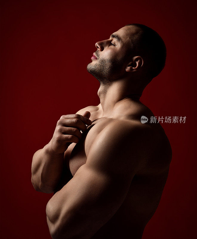 肌肉男人的肖像与完美的身体站在赤膊侧对着摄像机，头和眼睛关闭