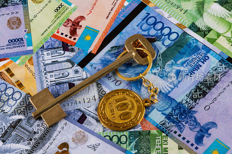 带有钥匙链的金钥匙，面值为100哈萨克铜币，背景是哈萨克纸币