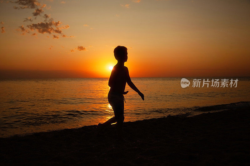 一个夏天的傍晚，一个年轻的男孩站在沙滩上，落日的光芒映在男孩的肩膀上