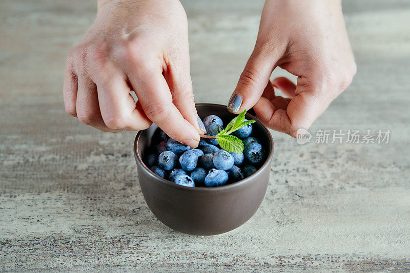 女性的手把新鲜的薄荷放在碗上面的蓝莓