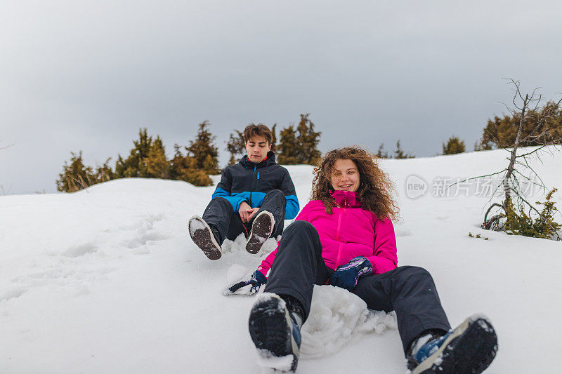 一对美丽的年轻夫妇坐在雪橇上从山上滑下来，在雪地里玩得很开心