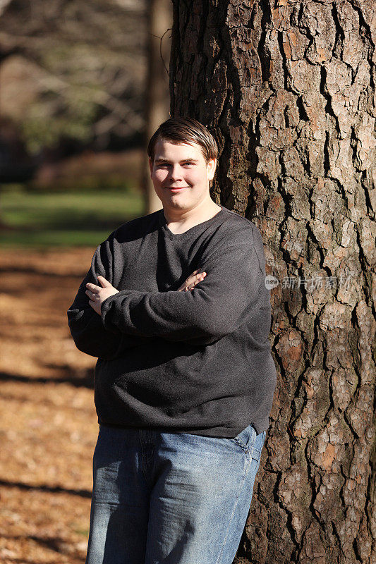 自闭症少年站在公园的一棵树上。