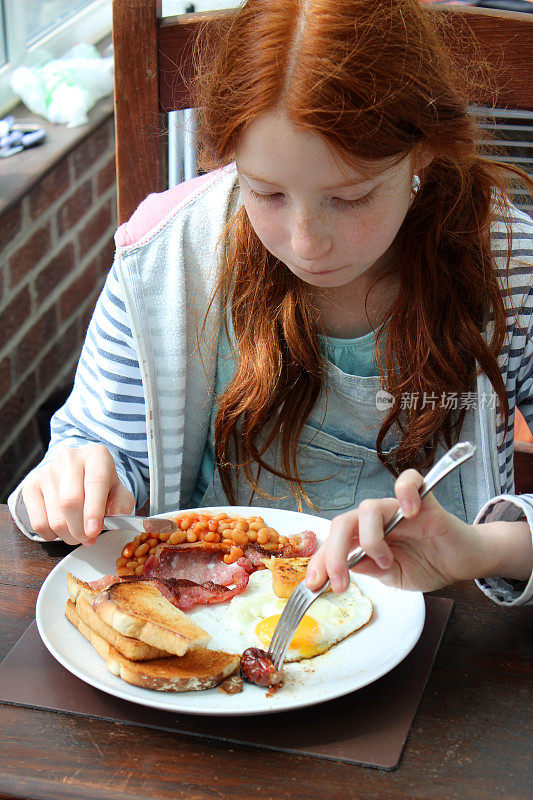 一个女孩吃着英式油炸早餐，烤豆子，香肠