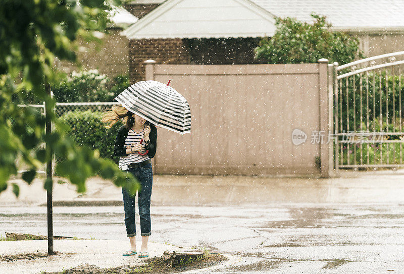 少女撑着伞在雨中走在街上。纽约皇后区