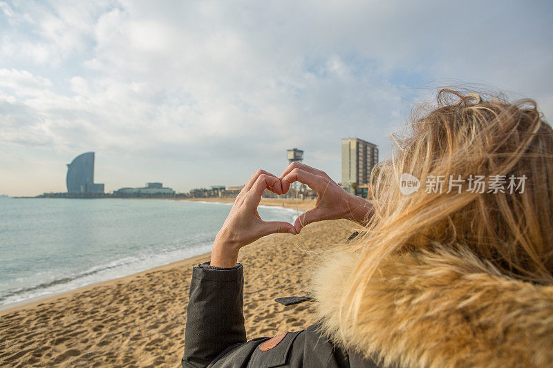 在巴塞罗那的海滩上，一名年轻女子正在做心形蛋糕