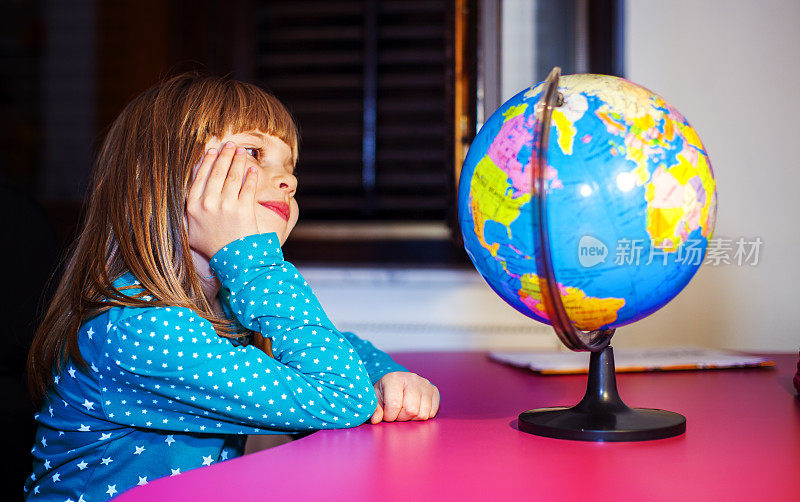 小女孩拿着地球仪坐在办公桌前