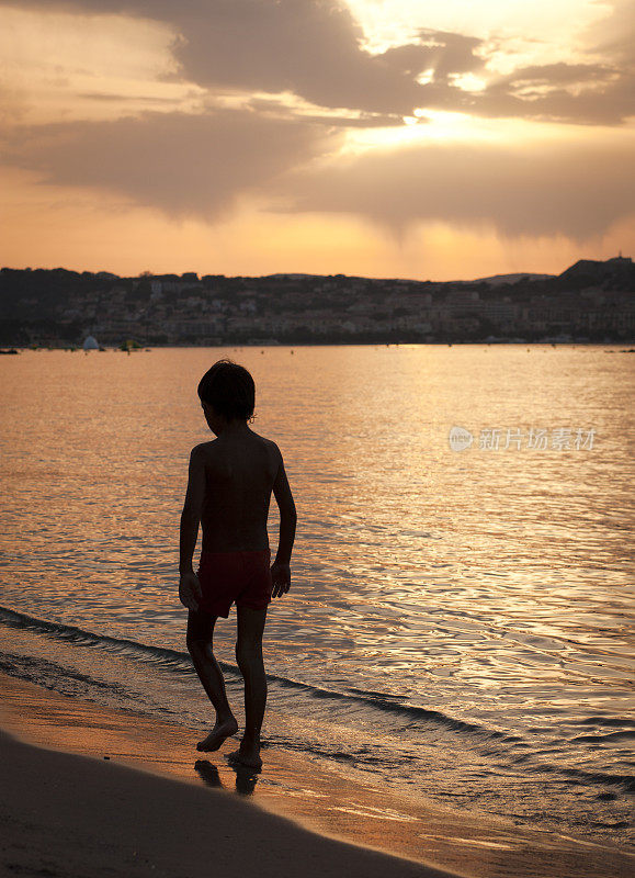 小男孩走在海边在日落，垂直