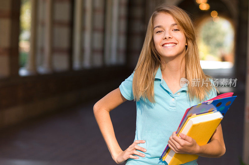 十几岁的女学生与手在臀部拿书在校园