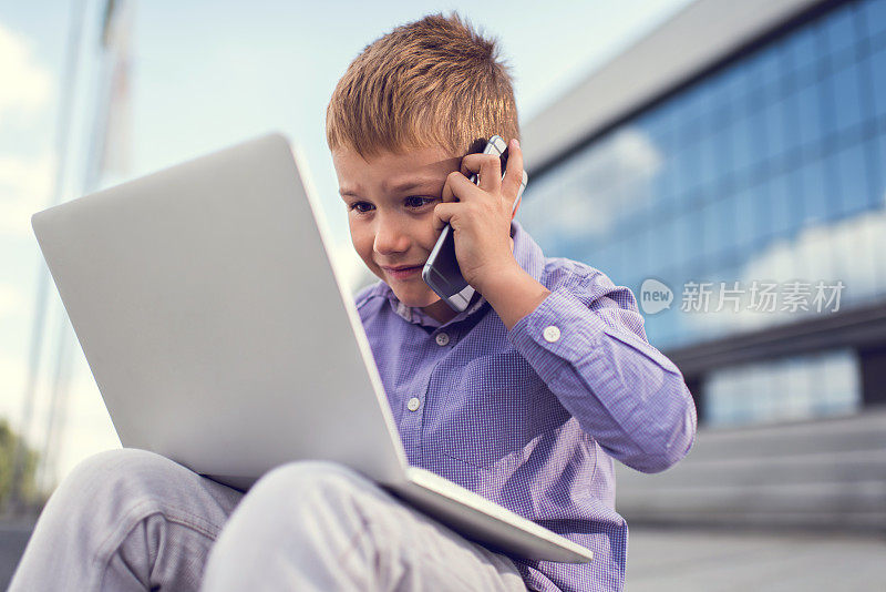 忙碌的商业男孩一边用笔记本电脑一边打电话。