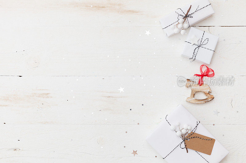 俯视图上漂亮的圣诞礼物包裹在白色的礼物纸，圣诞树装饰在白色的木制背景与闪闪发光的星星。新年、假期和庆祝概念