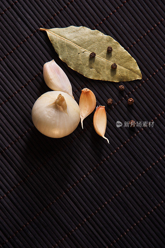 大蒜，洋葱，月桂叶，黑胡椒在黑色的桌上。食品的背景。蒜。大蒜片，蒜瓣，蒜头。
