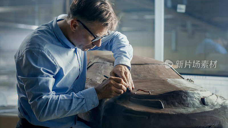 高级汽车设计师与Rake雕刻未来汽车模型从橡皮泥粘土。他在一家大型汽车厂的专门工作室工作。