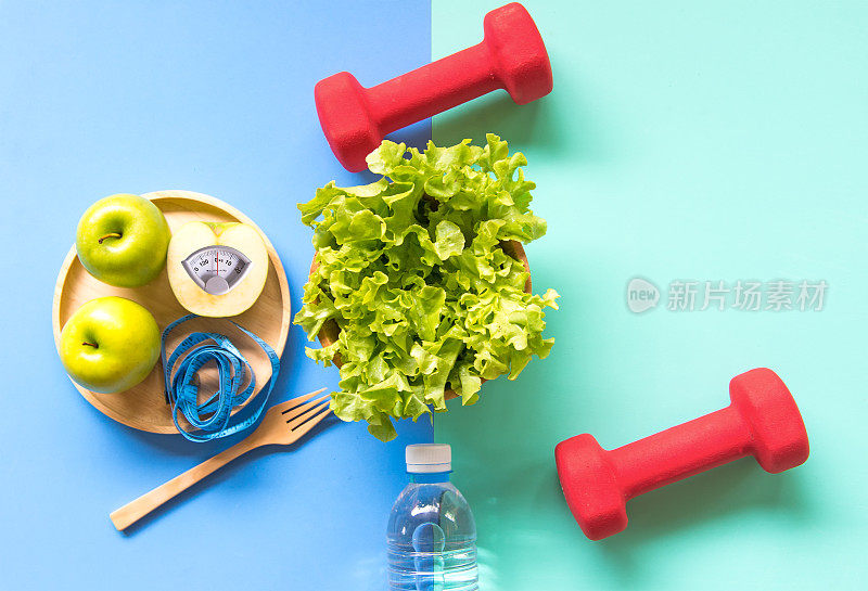 节食减肥用青苹果和计量水龙头，称重量的木板上，蔬菜，哑铃，彩色背景。饮食与健康理念