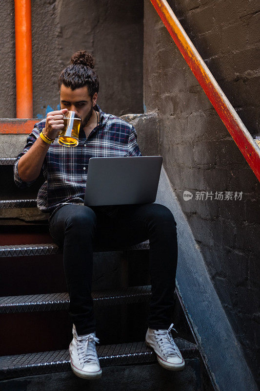 一个男人在楼梯上喝着啤酒，用着笔记本电脑