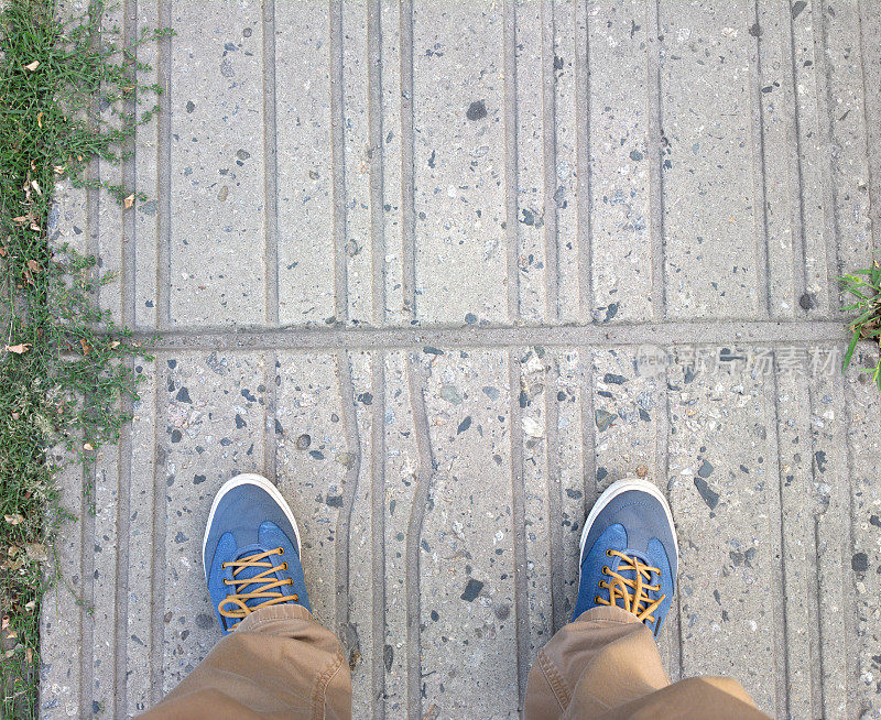 一个穿着蓝色球鞋的男人走上了正轨。脚放在瓷砖上。