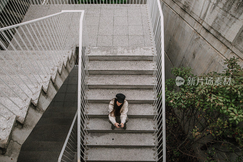 年轻女子拿着智能手机坐在楼梯上