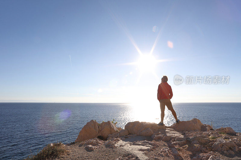 在海浪和阳光下，一个人站在岩石码头上