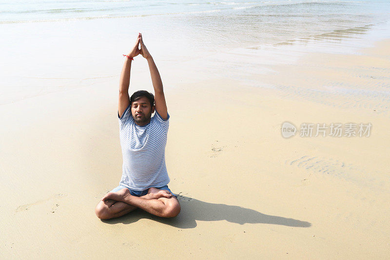 印度男子练习莲花姿势举起手臂(莲花手举起手臂)瑜伽姿势在潮湿的沙滩上，水的边缘，帕洛伦海滩，果阿，印度