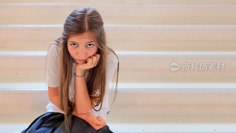 一个十几岁的女学生悲伤地坐在学校的台阶上。
