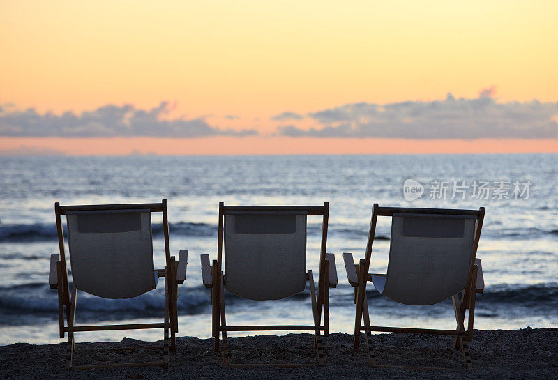 日落时分沙滩上的三把折叠椅