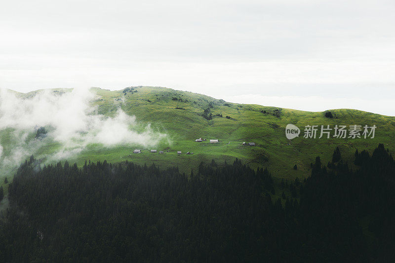 在瑞士阿尔卑斯山的夏季雨天，从山顶俯瞰被雾覆盖的山村和绿色草地