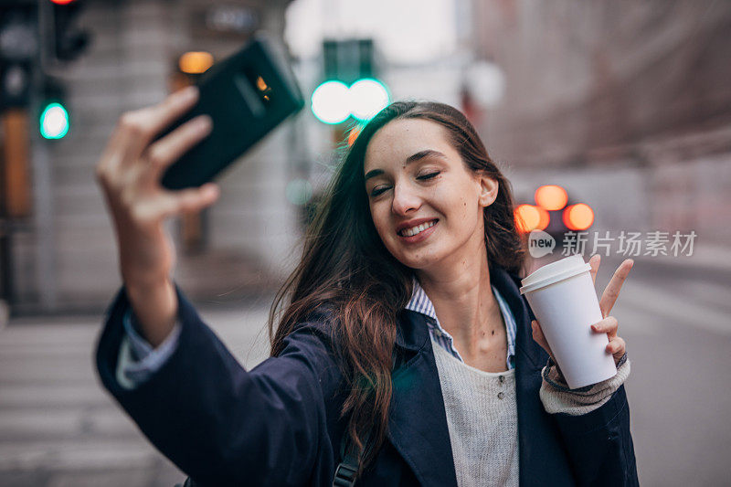年轻女子拿着一杯咖啡用智能手机自拍