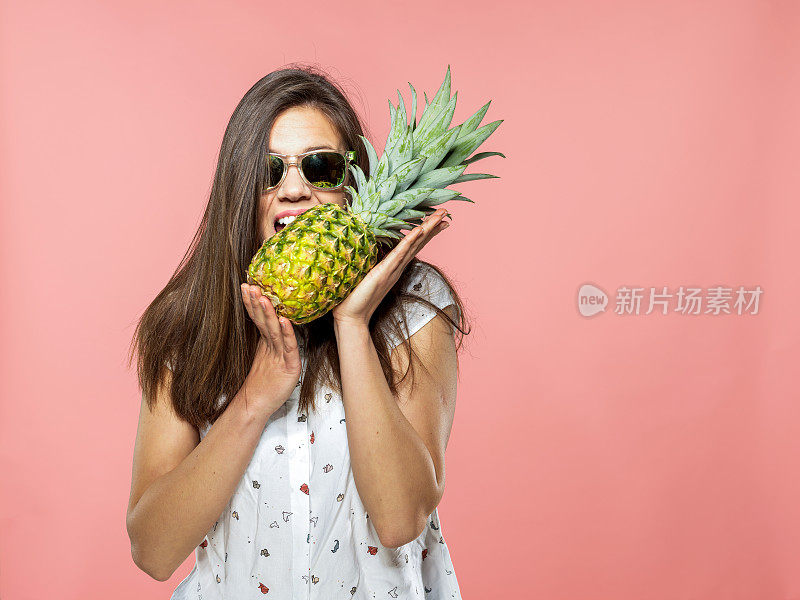 年轻女子戴着太阳镜咬在菠萝在珊瑚的背景