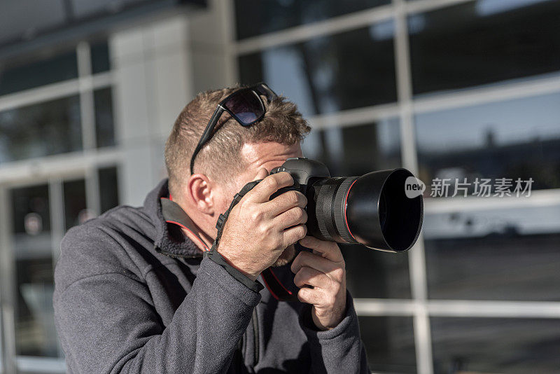 旅行者成年男子在城市里用专业相机拍照