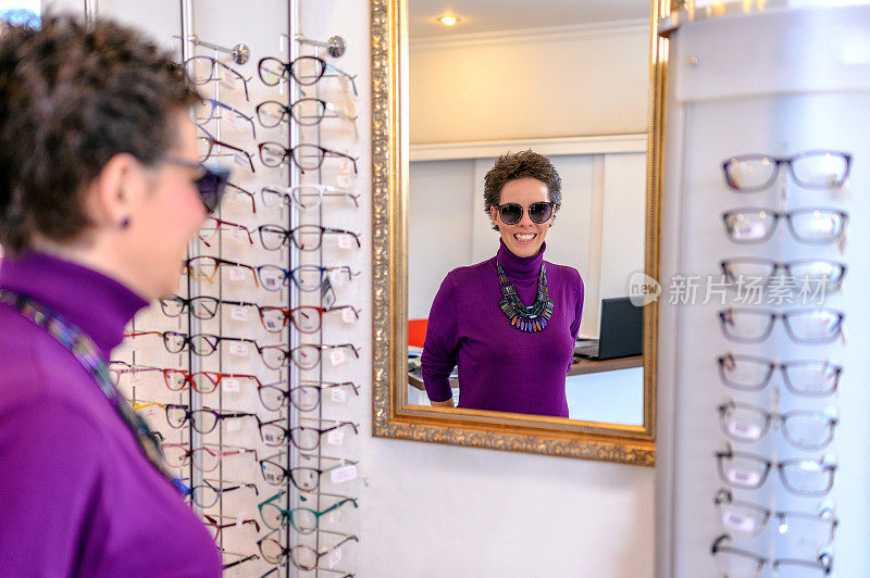 微笑的女人在眼镜师的镜子上试太阳镜。