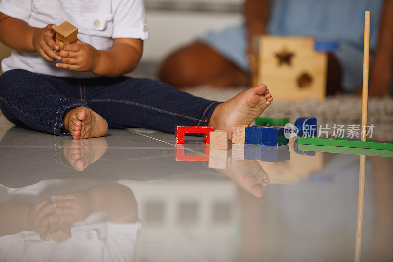 剪出一只脚的小男孩坐在地板上玩着五颜六色的玩具