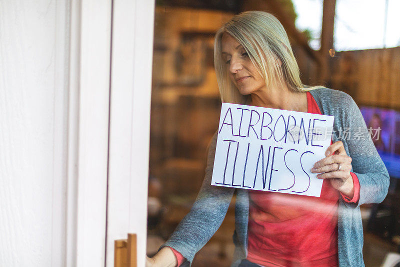 在空气传播疾病危机期间，在隔离期间，成熟女性在家避难所手持标志图像系列