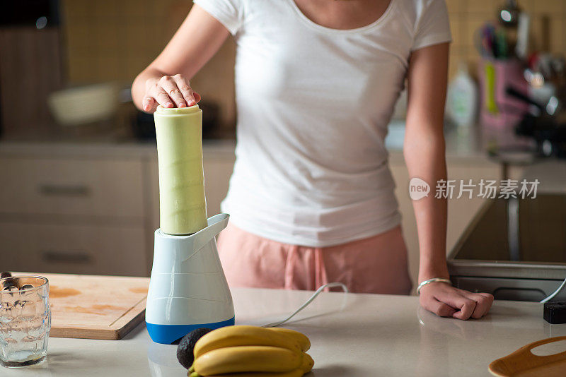 一个女人正在做鳄梨和香蕉奶昔作为健康的早餐饮料