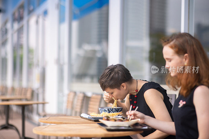 两个白人妇女在户外咖啡厅吃乌冬和章鱼烧午餐