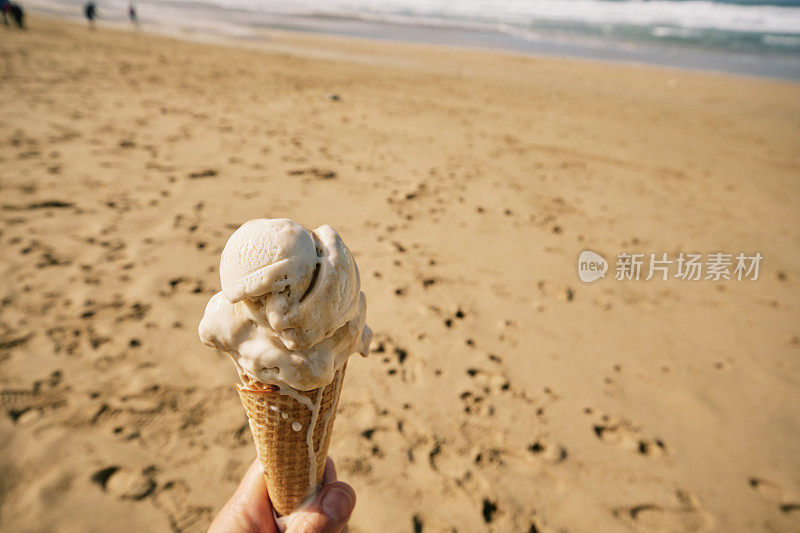 10月一个阳光明媚的日子，康沃尔纽基的菲斯特拉海滩，一只手拿着一个正在融化的焦糖味冰淇淋。