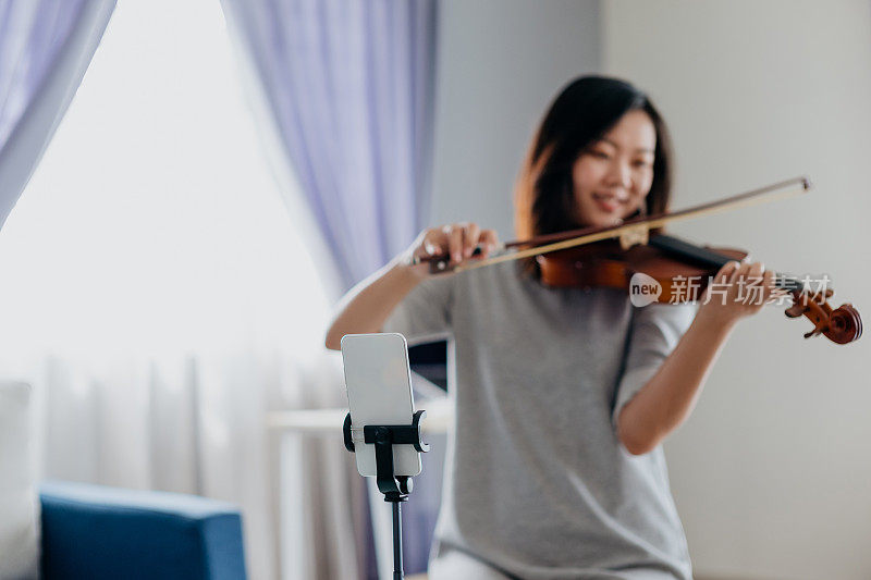 一名亚裔中国女子在用智能手机拉小提琴并进行直播