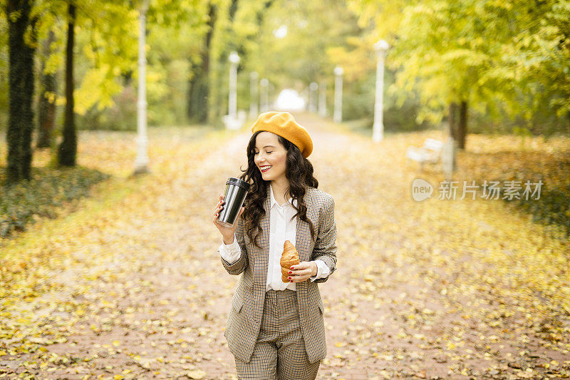 年轻的时尚女士微笑着，休息一下，吃零食，吃牛角面包，喝咖啡