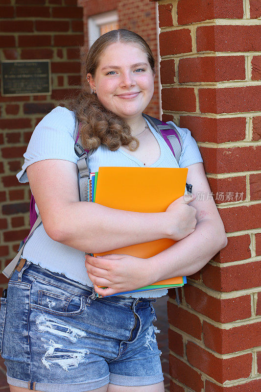 14岁的女孩阅读为回学校摆姿势与她的笔记本和背包。