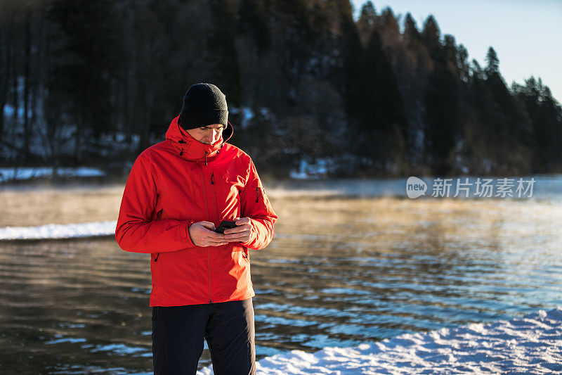 一名男子在湖边使用智能手机。