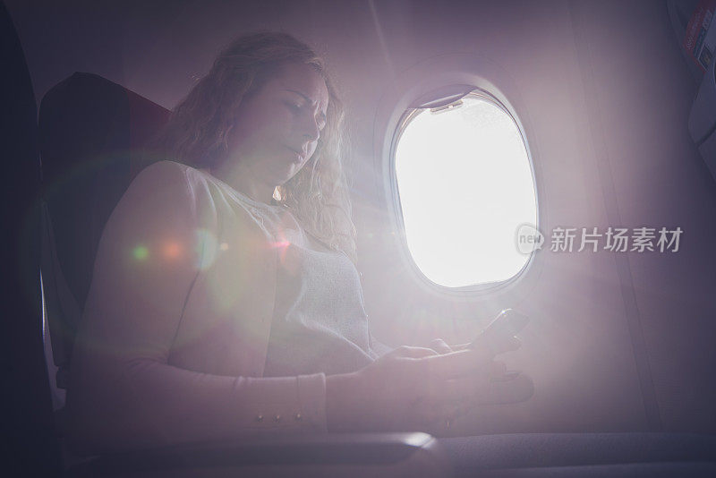 卷毛女人在飞机上用手机看她最喜欢的电影。