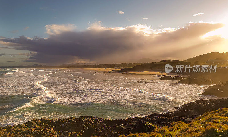 在澳大利亚东部，美丽的天然海滩和海岸风光在下午晚些时候的阳光透过正在逼近的风暴云层照射下来。