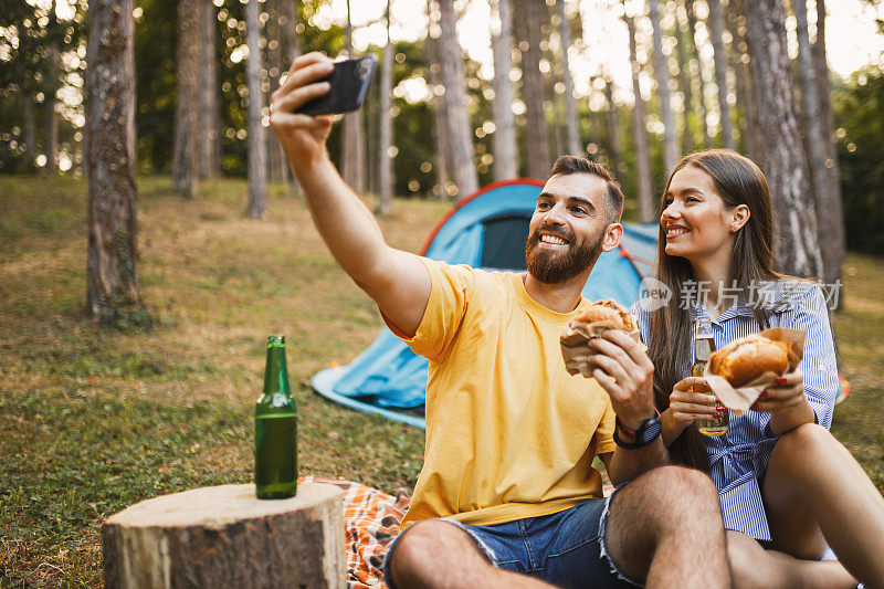 年轻夫妇在野外视频通话、露营、喝啤酒和吃汉堡