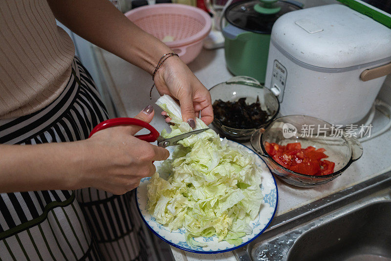 一名妇女正在用剪刀切白菜，双手特写