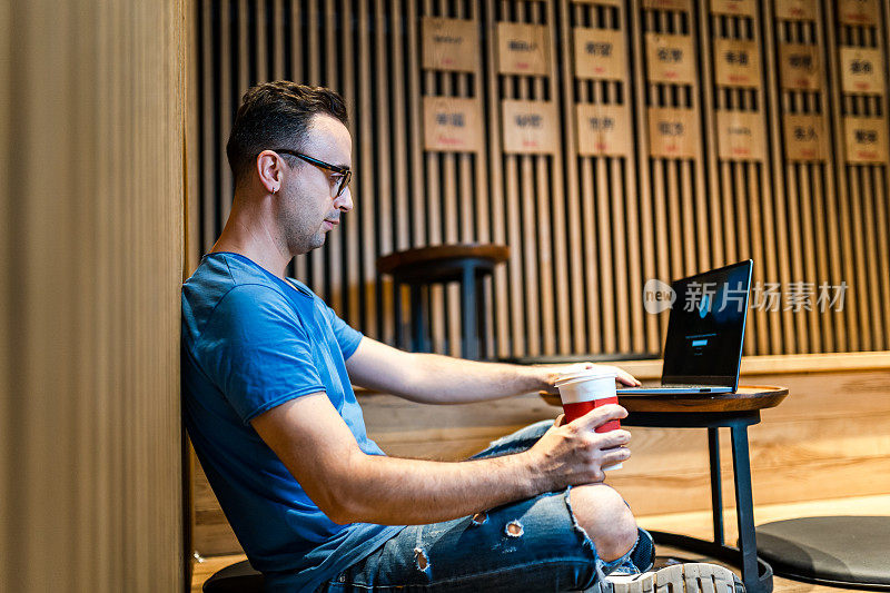 年轻人一边在咖啡店喝咖啡，一边用笔记本电脑工作