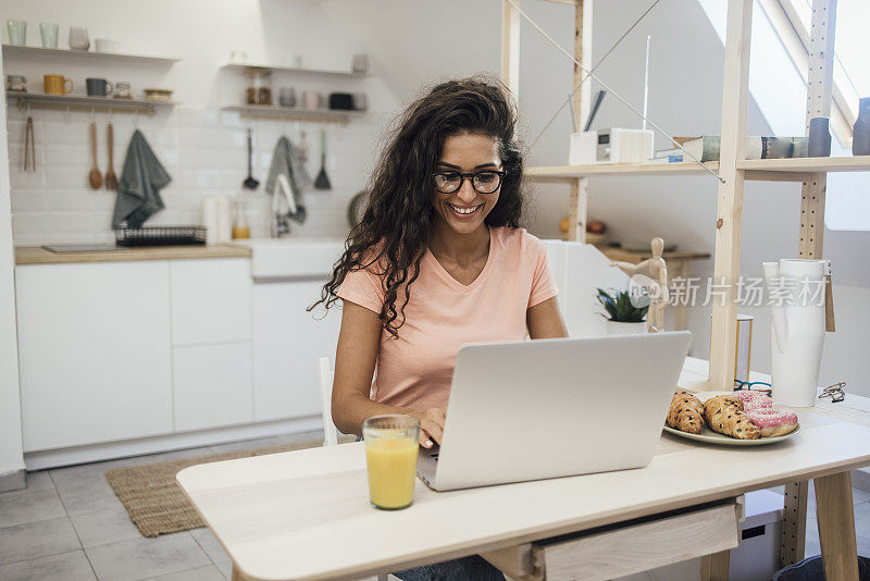 一个快乐的年轻女人在家里用笔记本电脑工作