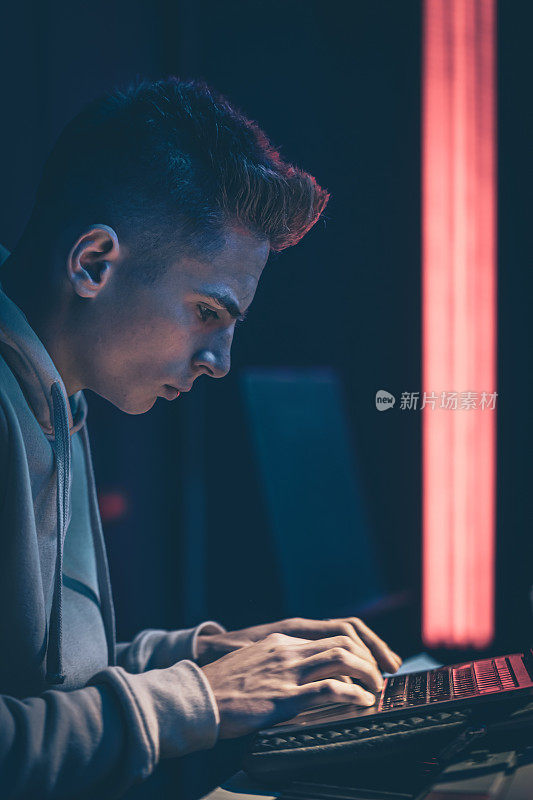 一个年轻人在黑暗的房间里用笔记本电脑敲着音乐键。