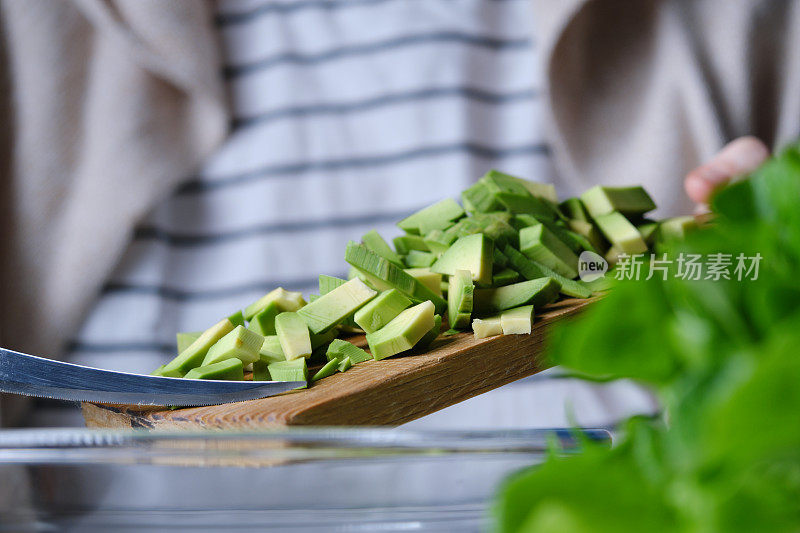 人手正在用生菜、芹菜茎、青苹果、橙子和鳄梨准备生沙拉