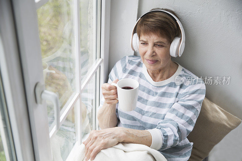 音频愈合。概念没有压力。老妇人戴着耳机听音乐，在家喝茶